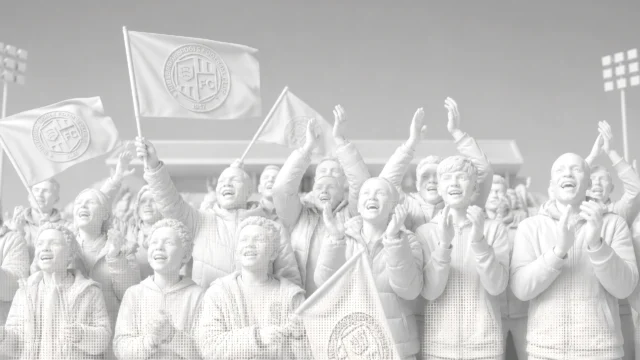 Cheering crowd of fans at a stadium, waving flags bearing a football club emblem.
